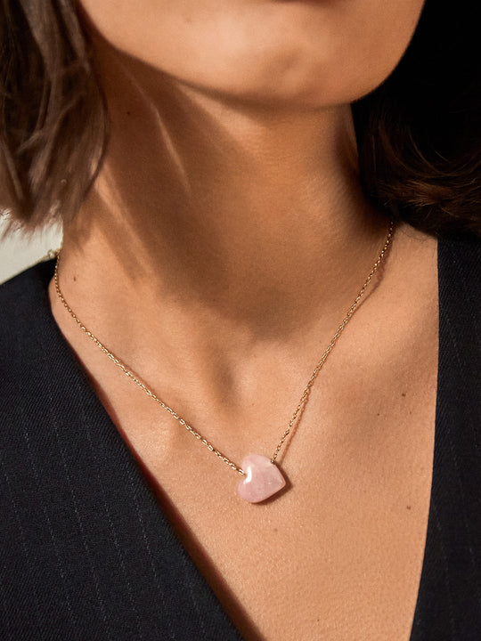 a person earing a necklace with a gold chain and a pink heart stone